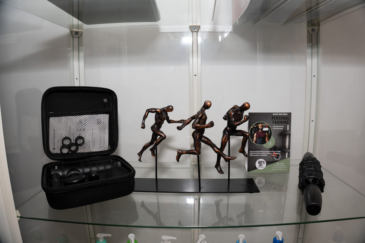 Display cabinet with massage tools, running figurines, and Heaven's Touch personal training card