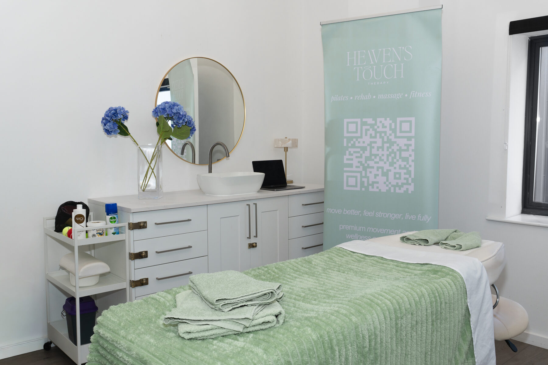 Heaven's Touch Therapy treatment room with sage branded banner, treatment bed, and vanity area
